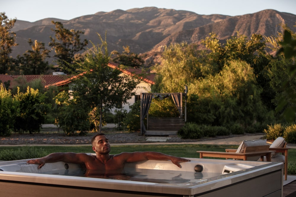 a man is relaxing in a jacuzzi j-lx hot tub with a mountain view
