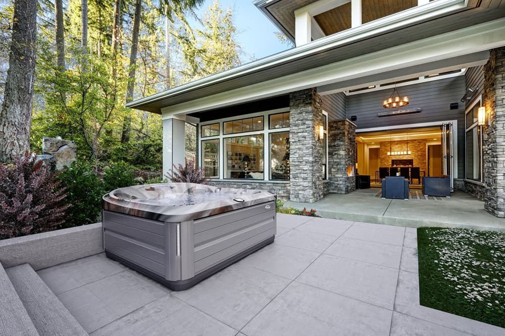 luxurious outdoor living space featuring a modern hot tub, stone accents on the house exterior