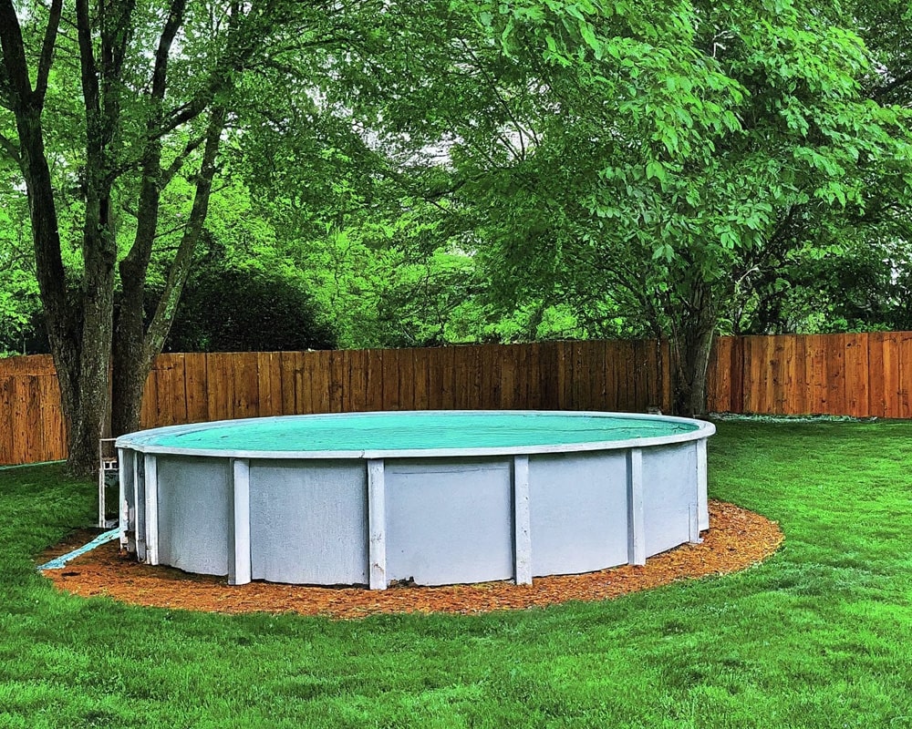 installed above ground pool in a green yard with trees and a fence.