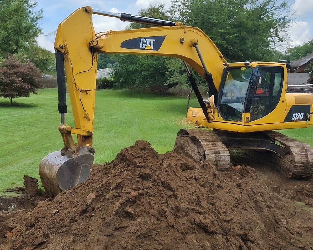 Yellow excavator digging up soil in a green field for swimming pool