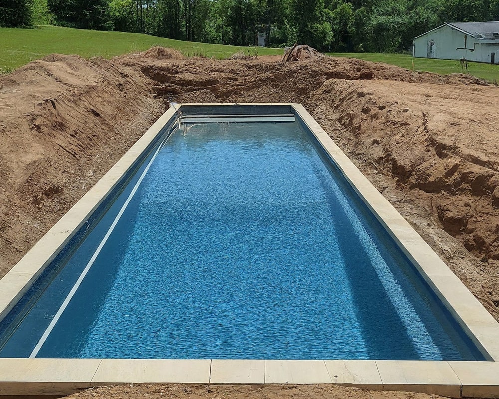 Newly installed rectangular swimming pool, surrounded by freshly dug earth in a backyard