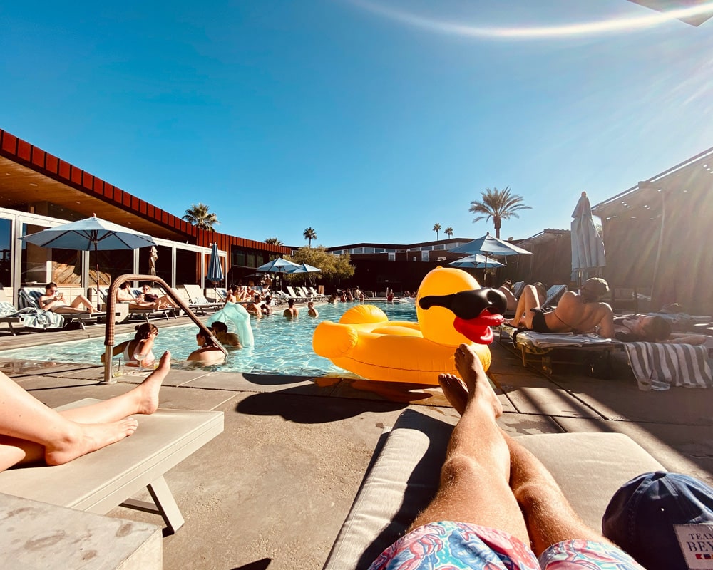 People enjoying a sunny day at a lively poolside with a giant inflatable yellow duck float